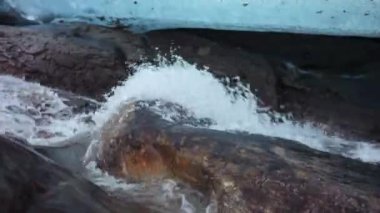 Yavaş çekim. Buzulun eriyen akıntısının yakın görüntüsü buzulun buzul alanının altından akıyor..