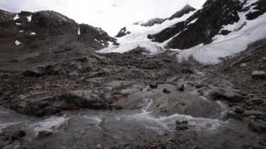 Yaz mevsiminde Alp manzarası. Eriyen buzul su akıntısı yokuş aşağı akıyor. Buzul Vinciguerra ve arkadaki kayalık dağlar.