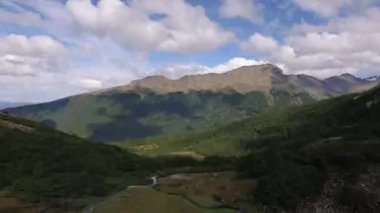 Yeşil ormanın, vadinin ve dağların güzel bir gökyüzünün altında havadan görünüşü. Buzul bir su akıntısı çayırlar boyunca akar..
