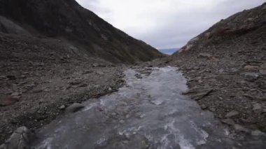 Andes kordillerasının yükseklerindeki kayalık dağların arasından akan buzullu su akıntısının görüntüsü.