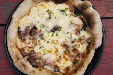 Restoranın ahşap masasında mozzarella peyniri, mantar, kıtır domuz pastırması, dilimlenmiş soğan ve sarımsaklı pizza.. 