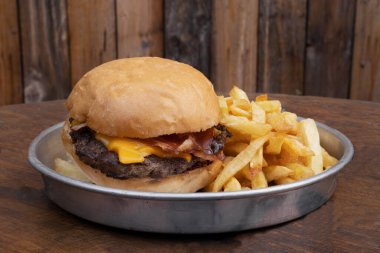 Burgerler. Restoranın ahşap masasındaki metal bir tabakta domuz pastırmalı peynirli hamburger ve patates kızartması.. 