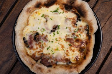 Restoranın ahşap masasında mozzarella peyniri, mantar, kıtır domuz pastırması, dilimlenmiş soğan ve sarımsaklı pizza.. 