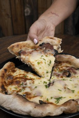 Pizza yiyorum. Lokanta ahşap masasında, peynirli, mantarlı, kızarmış pastırmalı, dilimlenmiş soğanlı ve sarımsaklı bir dilim pizza tutan kadın..