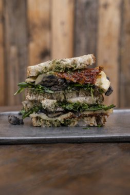 Vejetaryen sandviçi. Dilimlenmiş taze bir sandviçin yakından görüntüsü roka, kurutulmuş güneş domatesleri, peynir ve mantarlar, metal bir tabakta..