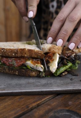 Restoranda yemek yiyorum. Kadının elinde bıçak, roka, güneşte kurutulmuş domates, peynir ve mantar dilimlenmiş vejetaryen sandviçi metal bir tabakta dilimlediği yakın çekim görüntüsü.. 