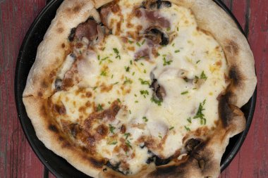 Pizza arka planı. Restoranın ahşap masasında mozzarella peyniri, mantar, kıtır domuz pastırması, dilimlenmiş soğan ve sarımsaklı pizza.. 