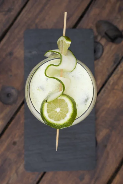 Cocktails. Top view of a gin tonic drink with lime and cucumber, on the bar wooden table.