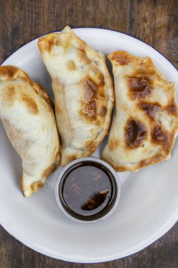 Ahşap masadaki beyaz kasede soslu üç et böreğinin yakın görüntüsü..