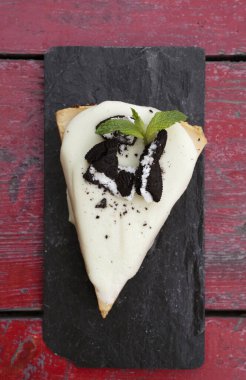 Tatlı tatlılar. Tahta masadaki siyah tabakta bir dilim pastanın en üst görüntüsü. Çikolata, kurabiye ve kremalı beyaz çikolatadan yapılmış bir pasta..