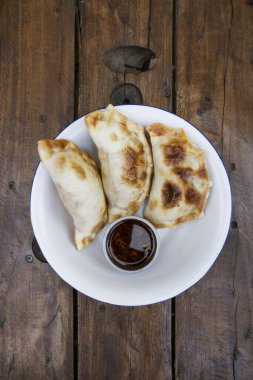 Ahşap masadaki beyaz kasede soslu üç et böreğinin yakın görüntüsü..