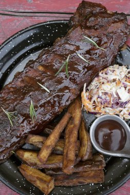 Barbekü sosu ve otlarla marine edilmiş domuz pirzolası, patates kızartması ve lahana salatası, kırmızı ahşap masada siyah bir tabakta.. 