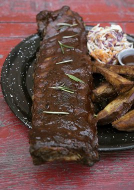 Barbekü sosu ve otlarla marine edilmiş domuz pirzolası, patates kızartması ve lahana salatası, kırmızı ahşap masada siyah bir tabakta.. 