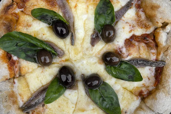 Top view of provolone and mozzarella cheese pizza with fresh basil leaves, black olives and anchovies.