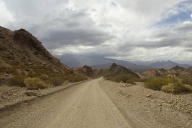 Hiçliğe giden kirli bir yol. Kayalık dağlardaki kurak çöl rotasında seyahat ediyorum..