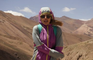 Güneş gözlüklü, dağlarda üşüyen genç bir kadın yürüyüşçü..