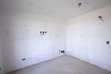 Gayrimenkul. Mimarlık. Boş oda yapım aşamasında. Köşe manzarası, beyaz duvarlar, beton zemin ve bitmemiş elektrik tesisatları. 