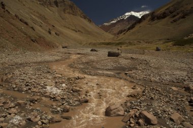 Vadi boyunca yokuş aşağı akan kayalık akarsu. Aconcagua Dağı, Amerika 'nın en yüksek zirvesi, arka planda..