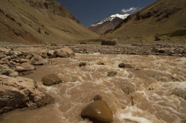 Vadi boyunca yokuş aşağı akan kayalık akarsu. Aconcagua Dağı, Amerika 'nın en yüksek zirvesi, arka planda..