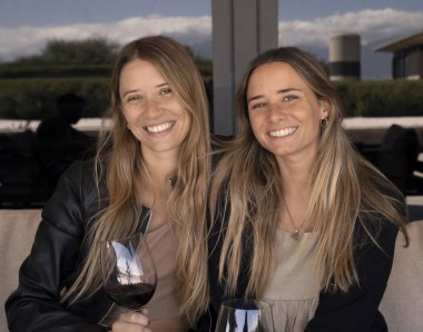 Arkadaşlar ellerinde kırmızı şarapla restoranda kameraya gülümsüyorlar..