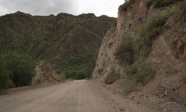 Seyahat et. Çöldeki toprak yola ve bulutlu gökyüzünün altındaki dağlara bakıyorum..