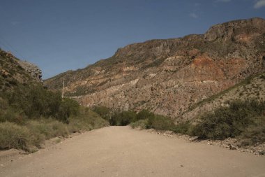 Seyahat et. Arjantin 'in Mendoza kentindeki Atuel Kanyonu' ndaki kurak çöl ve renkli kaya oluşumlarının üzerindeki toprak yol manzarası..