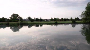 Gölün ve golf sahasının manzarası. Gölet turu, kıyı şeridi ve çim alanındaki ağaçlar. Su yüzeyindeki ağaçların ve gökyüzünün güzel yansıması..