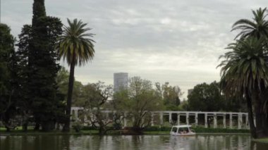 View of a lake in a public park. We can appreciate the palm trees and other plants as a small boat commonly used by tourists.