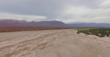Çölün havadan görünüşü, kum tepeleri, dağlar ve bitki örtüsü dramatik bir gökyüzü altında.