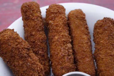 Kızarmış mozzarella çubuklarının üst görüntüsü kırmızı ahşap masadaki beyaz bir kaseye batırılmış barbekü sosu ile. 