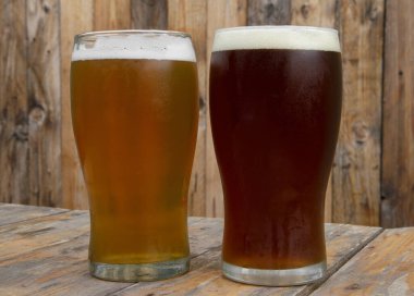 Bira. Barın ahşap masasındaki ahşap arka planda iki bira bardağının yakın görüntüsü. Altın bir bira ve kehribar birası.. 