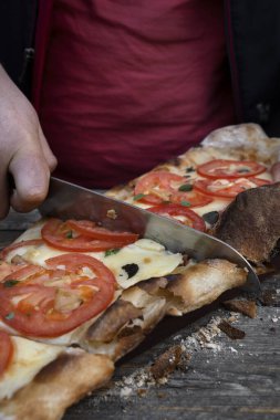 Bıçak tutan erkek, geleneksel bir Napoli pizzasını mozzarella peyniri, domates, sarımsak ve taze kekik yapraklarıyla dilimliyor.. 
