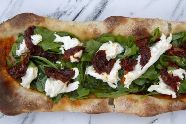 Gurme pizza. Beyaz mermer masada ev yapımı taze roka, İtalyan burrata peyniri ve kurutulmuş domates pizzası.. 