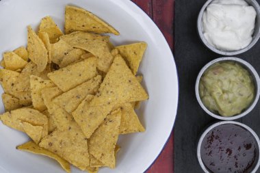 Meksika yemeği. Beyaz kasedeki nachos manzarası ve üç soslu çedar peyniri, acı biber ve guacamole, restoranın ahşap masasında.. 