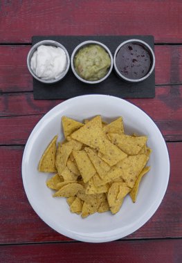 Meksika yemeği. Beyaz kasedeki nachos manzarası ve üç soslu çedar peyniri, acı biber ve guacamole, restoranın ahşap masasında.. 