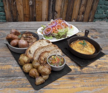 Geleneksel Arjantin yemekleri. Chorizos, domuz sosisi, ekmek, ızgara bağırsak ve provolone peyniri, criolla sosu ve ahşap masada servis edilen taze salata ile yakın çekim görüntüsü..  