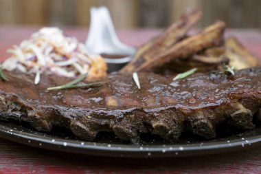 Lezzetli yemek. Barbekü sosu ve otla marine edilmiş domuz pirzolası, tatlı patates cipsi ve lahana salatası, masada siyah bir tabakta..