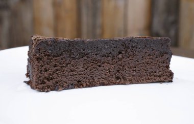 Tahta arka planda beyaz bir tabakta bir dilim browni..