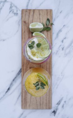 Mutlu saatler. Beyaz mermer masada iki meyveli kokteyl, tutkulu bir meyve kokteyli ve bir Campari, limon ve limon içeceği. Modern biçim sunumu.