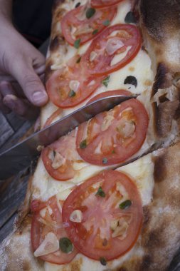 Bıçak tutan erkek, geleneksel bir Napoli pizzasını mozzarella peyniri, domates, sarımsak ve taze kekik yapraklarıyla dilimliyor.. 