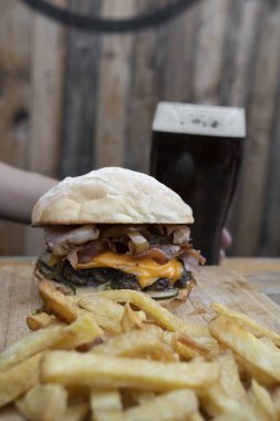 Fast food yiyorum. Çok katmanlı burger, kızarmış patates, garnitür ve koyu bira.. 