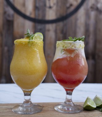 Beyaz mermer masada tropikal meyve kokteylleri, tutkulu bir meyve kokteyli ve bir Campari, ron ve limon içeceği yakından görülüyor..