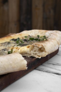 Gastronomi. Yakından bakınca, beyaz mermer masadaki ahşap tabakta mozzarella peynirli ve yeşil soğanlı mantarlı pizza dilimi görülüyor.. 