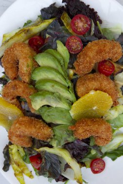 Beslenme ve diyet. Marul, lahana, domates, kızarmış karides, avokado ve portakallı renkli salata beyaz bir tabakta servis edilir..