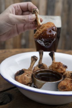 Yemek yiyorum. Yakından bakınca, acı-tatlı sosa batırılmış kızarmış tavuk kanadı tutan bir elin görüntüsü.. 