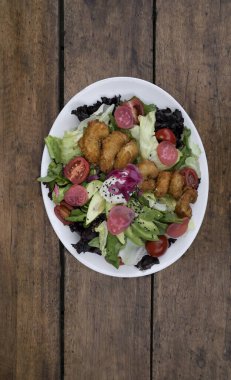 Gurme salatası. Marul, kiraz, domates, avokado, turp ve soğan turşusu, tohum ve krem peynirli deniz salatasının ahşap masada beyaz bir tabakta görüntüsü.. 