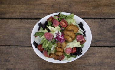 Gurme salatası. Marul, kiraz, domates, avokado, turp ve soğan turşusu, tohum ve krem peynirli deniz salatasının ahşap masada beyaz bir tabakta görüntüsü.. 