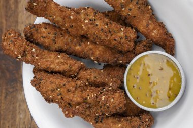 Kızarmış gurme yemeği. Tohumlu kızarmış tavuk çubukları ve hardal ve baldan yapılmış bir sos. Masanın üzerinde beyaz bir kâsede..