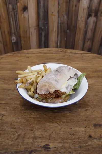 Closeup view of a chicken fried steak sandwich with lettuce, mayonnaise and french fries, in a white bowl on the wooden table.
