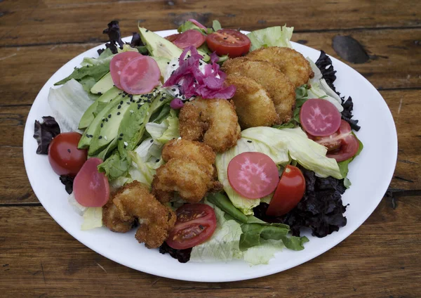 Gurme salatası. Marul, kiraz, domates, avokado, turp ve soğan turşusu, tohum ve krem peynirli deniz salatasının ahşap masada beyaz bir tabakta görüntüsü.. 